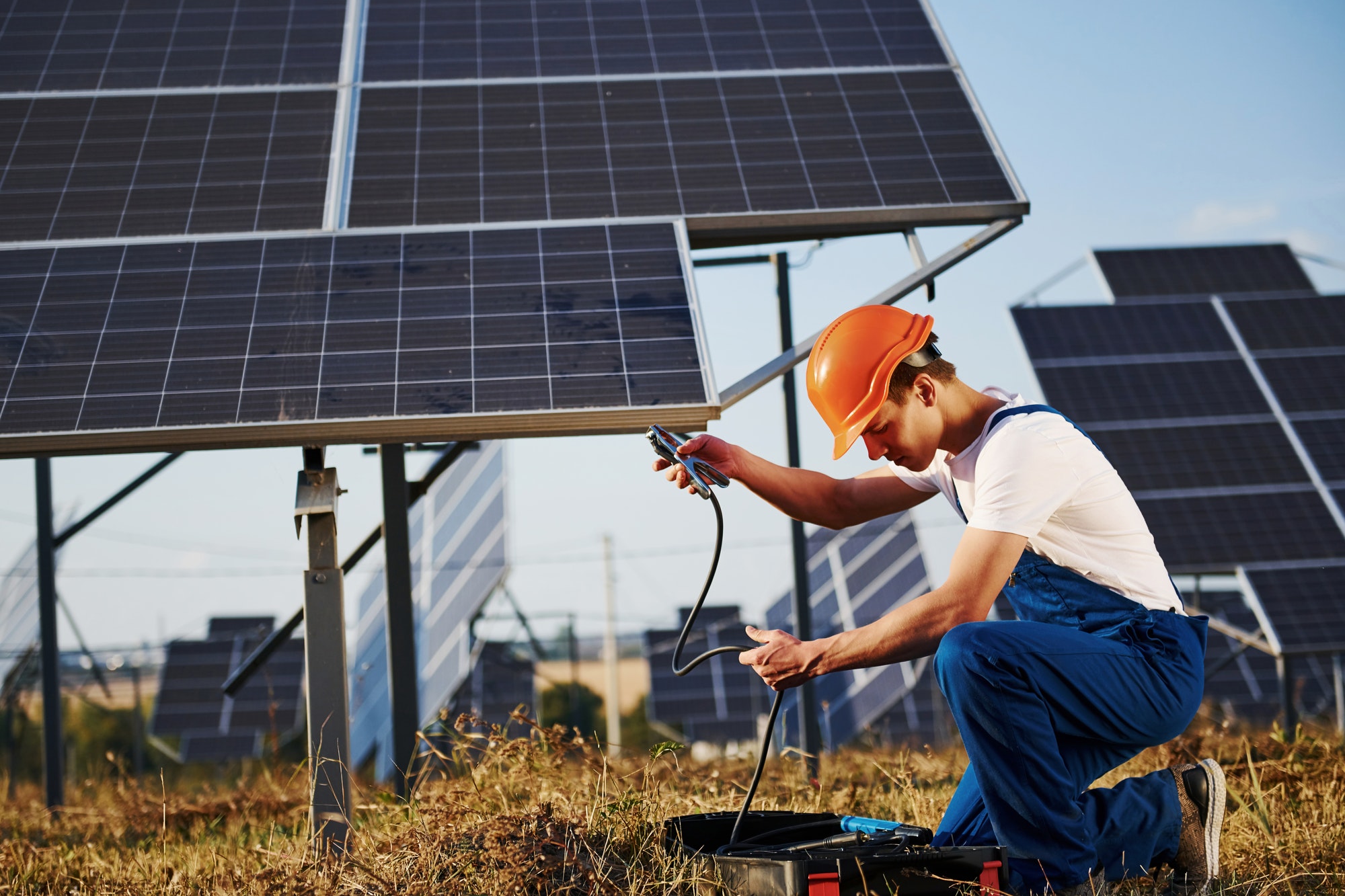 opening case with equipment male worker in blue uniform outdoors with solar batteries at sunny day